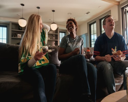 A family sitting together in a living room, smiling and holding tea mugs